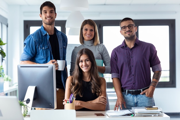 Shot of successful business team posing grouped around an attractive young woman looking at the camera in the coworking space.