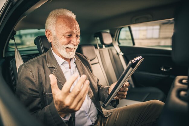 Shot of a successful senior businessman using digital tablet while sitting in the backseat of a car during his morning commute.