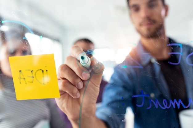 Shot of successful young man writing on office glass board during the meeting with colleagues in the coworking space.