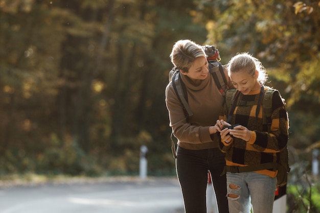 Shot of a teen girl and her mom using digital photo camera during walk together through the forest in autumn.