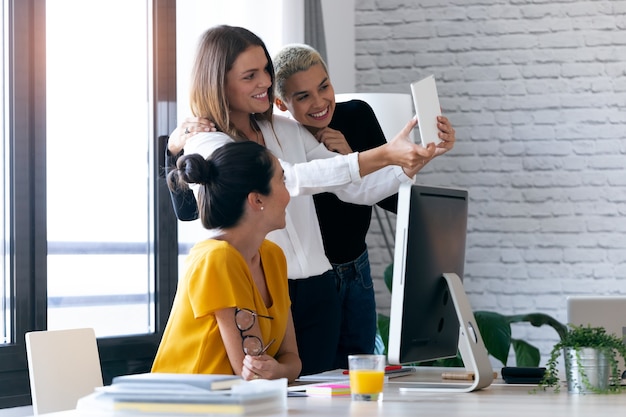 Shot of three modern businesswomen taking a selfie with digital tablet while working in the office.