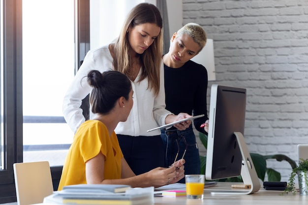 Shot of three modern businesswomen talking and reviewing the latest work done on the digital tablet in a joint workspace.