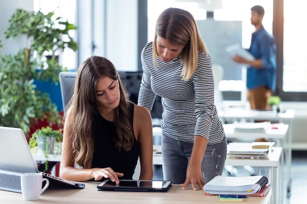 Shot of two business young women working together with digital tablet in the modern startup office.