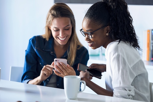 Shot of two pretty young business women using her mobile phone together while taking a break in the office.