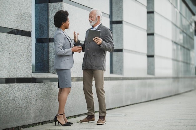 Shot of two successful multi-ethnic business people having a discussion during a quick break in front of the office building.