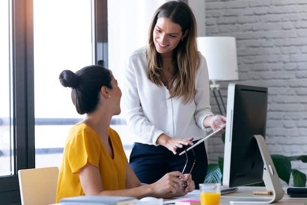 Shot of two young businesswomen talking and reviewing they last work in the digital tablet in the office.