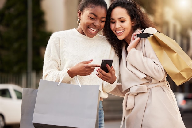 Shot of two young women using a smartphone while shopping against an urban background