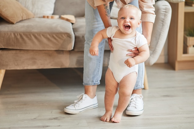 shot of unrecognizable woman wearing jeans helping her cheerful little kid with learning to walk