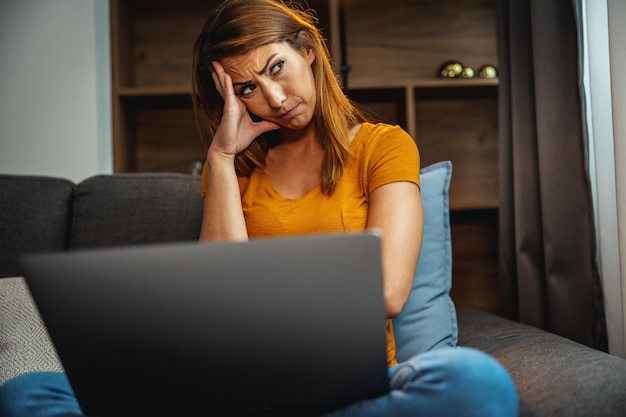 Shot of an worried young woman sitting cross legged on the sofa and using her laptop at home.