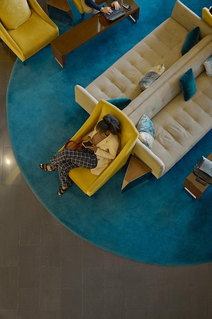 Above shot of young black woman with mobile gadget relaxing in lounge