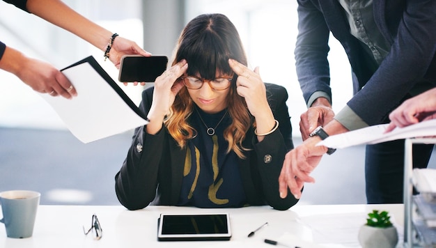 Shot of a young businesswoman looking stressed while being overwhelmed with requests from her colleagues in a modern office