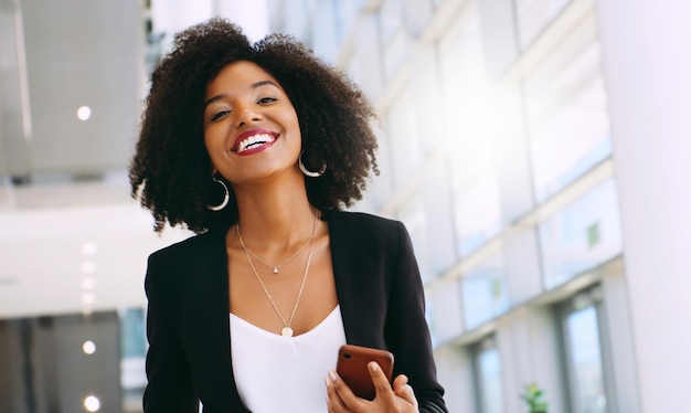 Shot of a young businesswoman using a smartphone while walking through a modern office