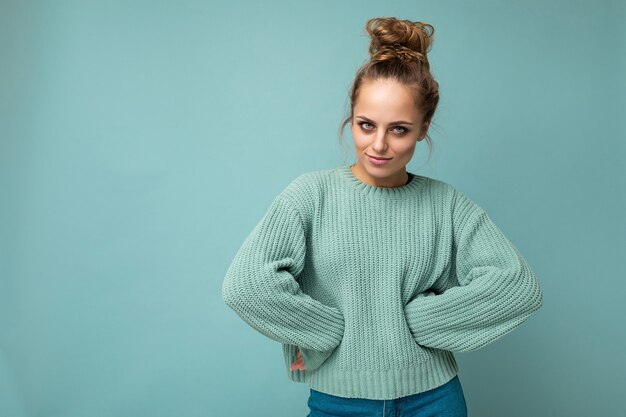 Shot of young happy pretty blonde woman wearing blue jersey isolated on blue wall with empty