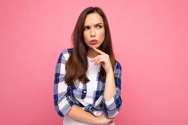 Shot of young thinking beautiful brunette woman with sincere emotions wearing trendy check shirt