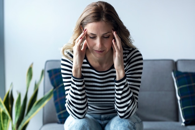 Shot of young woman with headache sitting on the sofa in the living room at home.