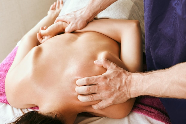 Shoulder area upper back and neck deep stroking and pressure tissue massage young white woman receiving physiotherapy while lying face down on massage table