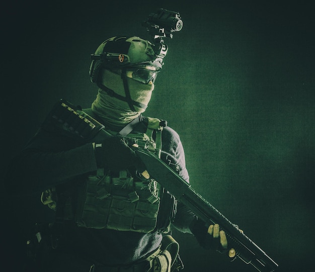 Shoulder portrait of army elite troops soldier antiterrorist tactical team wit shotgun helmet with thermal imager hiding face behind mask armed rifle with optical scope studio shoot on black