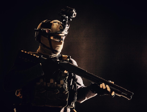 Shoulder portrait of army elite troops soldier antiterrorist tactical team wit shotgun helmet with thermal imager hiding face behind mask armed rifle with optical scope studio shoot on black