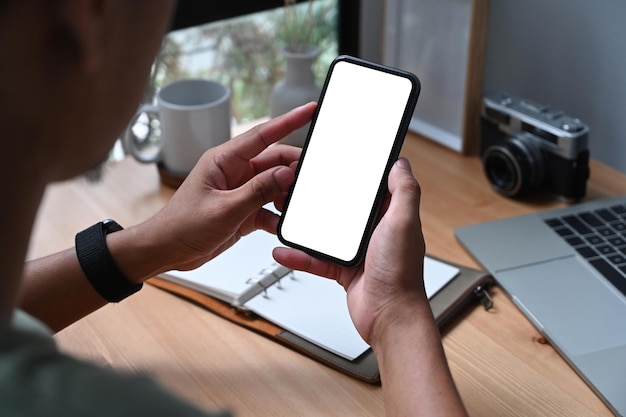 Over shoulder view of young asian man holding smart phone with empty screen.