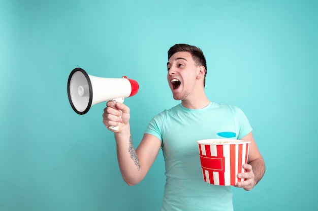 Shouting with popcorn. Caucasian young man's portrait isolated on blue  wall. Beautiful male model in casual style, pastel colors. Concept of human emotions, facial expression