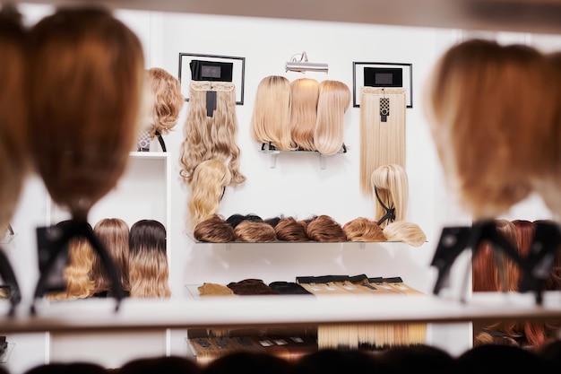 Showcase of natural looking wigs in different colors fixed on the metal wig holders in beauty salon Row of mannequin heads with variation shades hair on shelf in wig shopxA