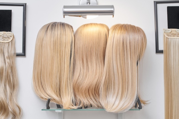 Showcase of natural looking wigs in different shades of blonde fixed on the wig holders in beauty salon Row of mannequin heads with variation colors fair hair on shelf in wig shop