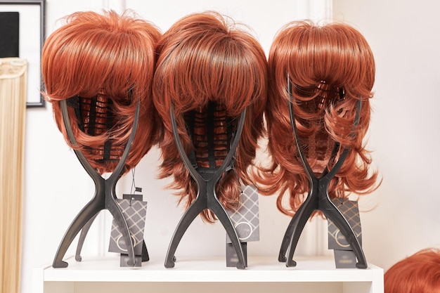 Showcase of natural looking wigs in different shades of brunette fixed on the wig holders in beauty salon Row of mannequin heads with variation colors hair on shelf in wig shop