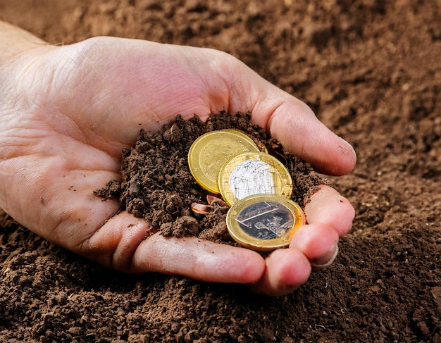 showing a hand gripping the ground with several coins sandwiched between the fingers