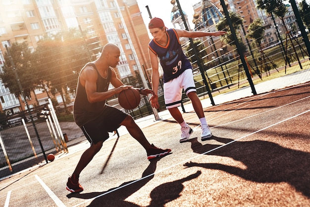 Showing his skills. Two young men in sports clothing playing basketball while spending time outdoors