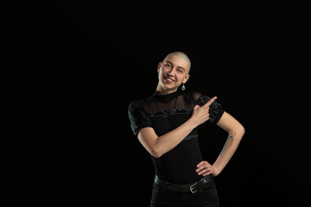 Showing something. Monochrome portrait of young caucasian bald woman isolated on black studio wall.