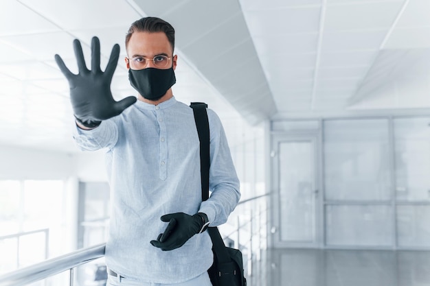 Showing stop gesture by hand In protective mask and gloves Young handsome man in formal clothes indoors in the office at daytime