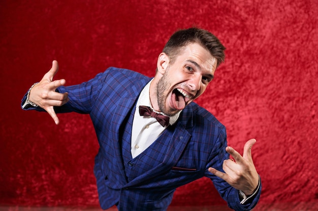 showman in suit showing tongue and rock gesture while looking at camera