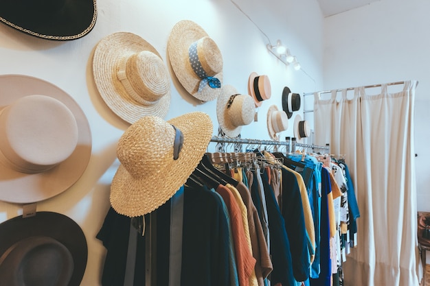 Showroom store of women's clothing and summer straw hats hang on the wall. Rack hanger with colorful outfits. Modern minimalistic interior