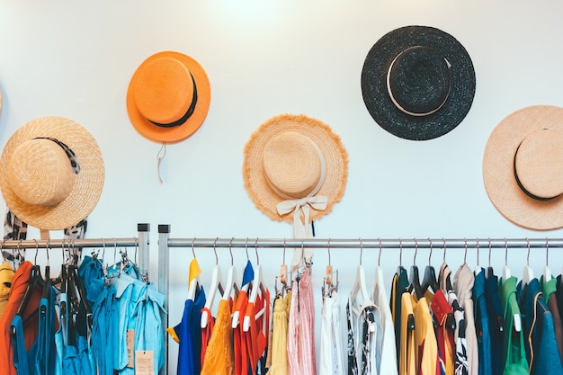 Showroom store of women's clothing and summer straw hats hang on the wall. Rack hanger with colorful outfits. Modern minimalistic interior