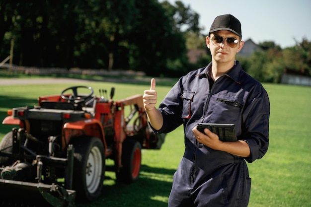 Shows thumb up Man is with utility tractor with grass cutter and aerator equipment on the field