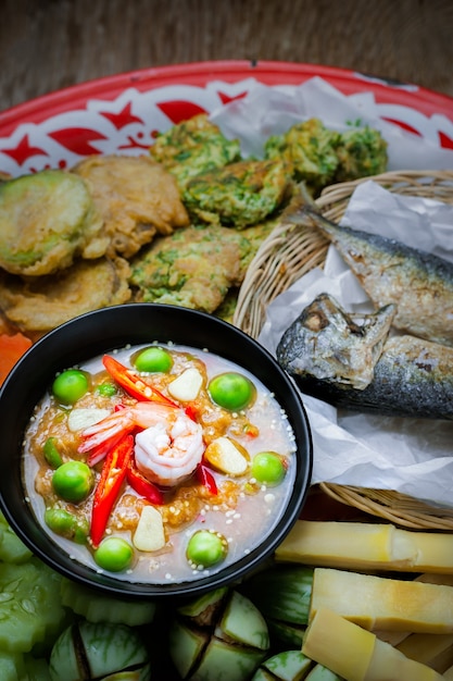 Shrimp - paste sauce with vegetables, omelet, fried mackerel  on wooden table. 