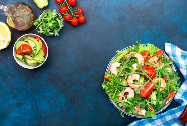 Shrimp salad with tomatoes lettuce arugula avocado cucumber and lemon dressing on blue table Healthy eating clean food concept Top view