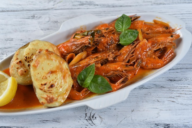 Shrimp with tomato sauce, baked potato, lemon and basil on a white fish-shaped plate