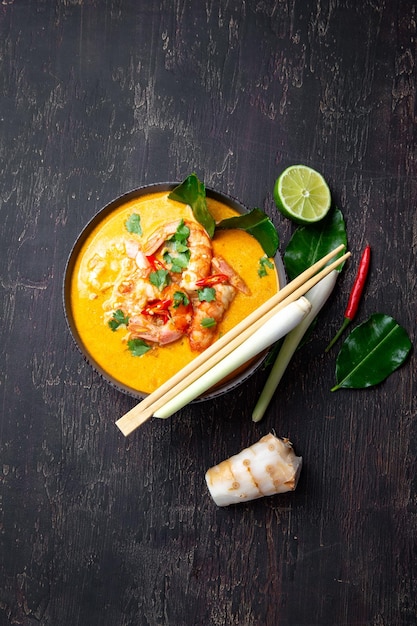 Shrimps Tom Yam Kung in grey bowl with thai spices on autentic tray top view wooden background