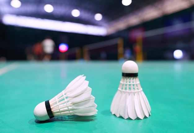 Shuttlecock on green badminton playing court with player in background