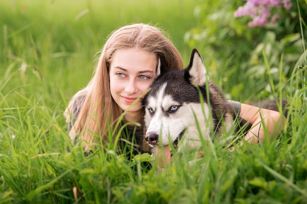 A Siberian Husky and his beautiful blueeyed owner are cuddling while lying in the grass The concept of love for animals and nature