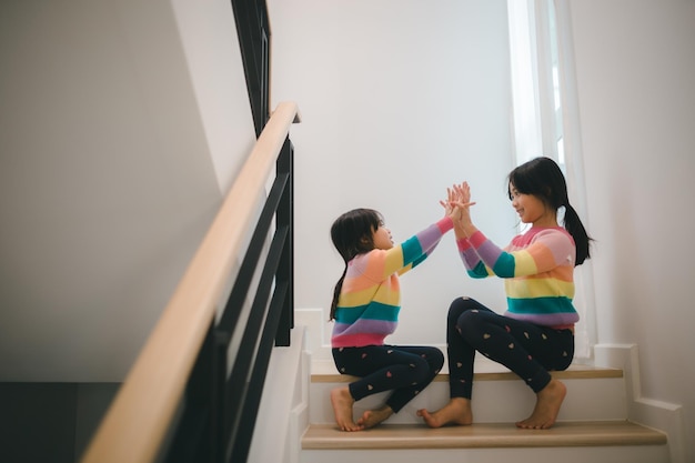 Sibling Asian girls playing rock paper scissors hand game children sitting on stairs at home playing together