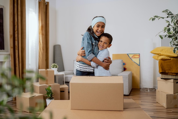 Siblings hugging girl and boy cooperating helping parents with packing things for moving