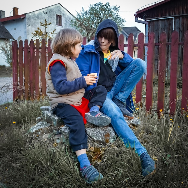 Photo siblings sitting on rock in yard