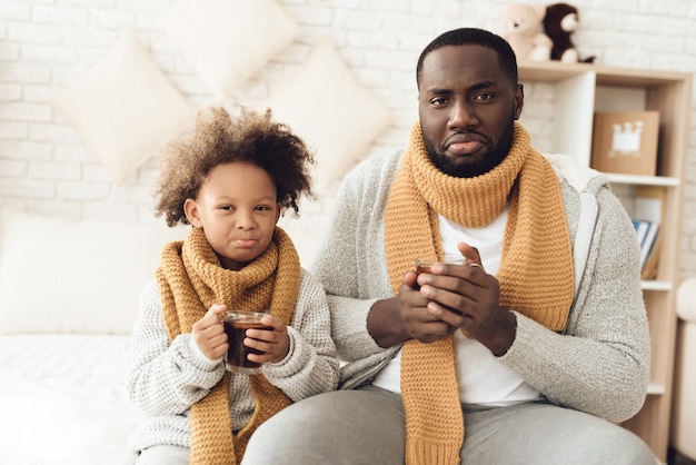 Sick African American father and daughter drinking tea.