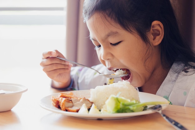 Sick asian child girl eating healthy food for lunch by herself while stay in private patient rooms in the hospital. Healthcare and lifestyle concept.