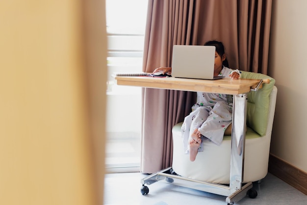 Sick asian child sitting and learning online class with teacher and friend while stay in private patient rooms in the hospital. Isolation homeschooling and distance learning.