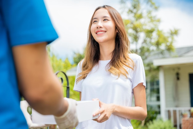 Sick Asian young woman receive medicine first aid pharmacy box from hospital delivery service, happy female receiving patient medicine drug from delivery man, healthcare medicine online concept