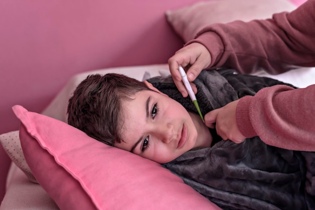 Sick boy with thermometer laying in bed and mother hand taking temperature mother checking temperatu