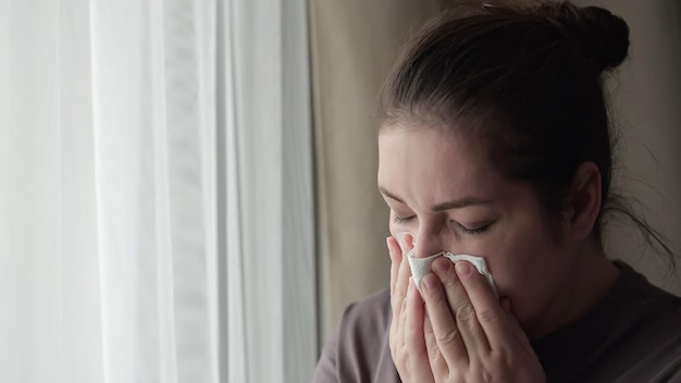 Sick brunette woman sneezes covering nose with napkin